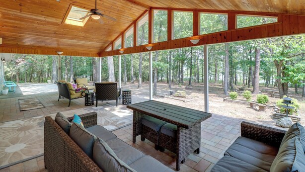 An open-plan living area with a wooden ceiling, large windows, and outdoor views of a forest. - Arkansas Vacation Rental on Greers Ferry Lake! (Higden)