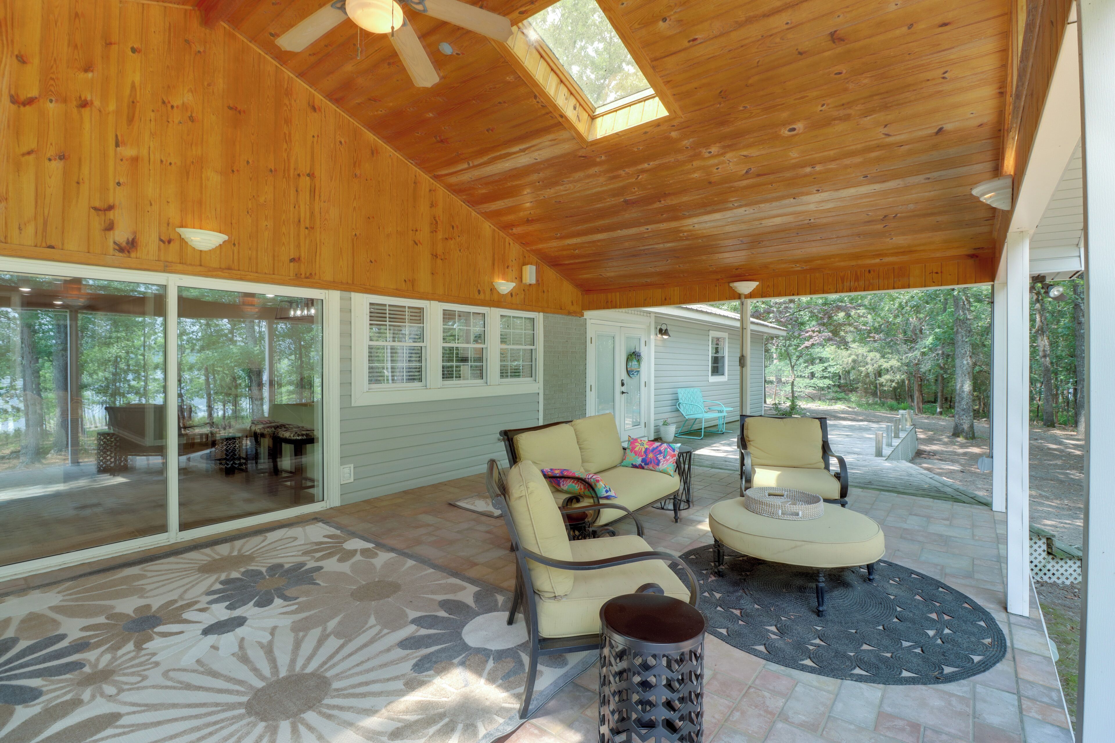 Une terrasse couverte avec un plafond en bois, de grandes fenêtres et du mobilier d’extérieur.