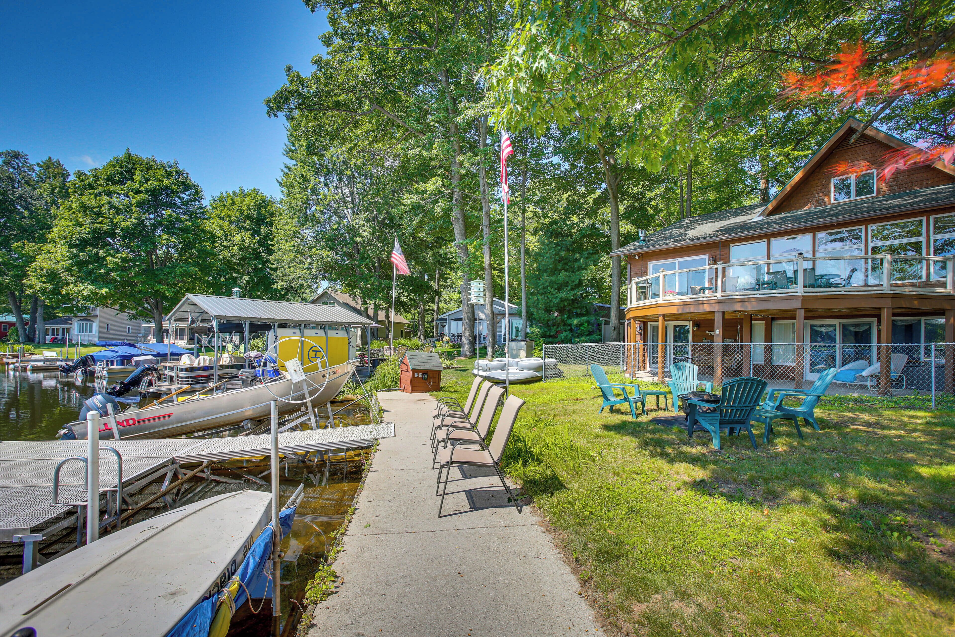 A lakeside dock with boats, a grassy area with chairs, and a building with large windows.