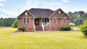 A two-story brick house with a front porch, a covered porch area, and a well-maintained lawn. - Peaceful Getaway in Blonts Creek Near Washington (Blounts Creek)