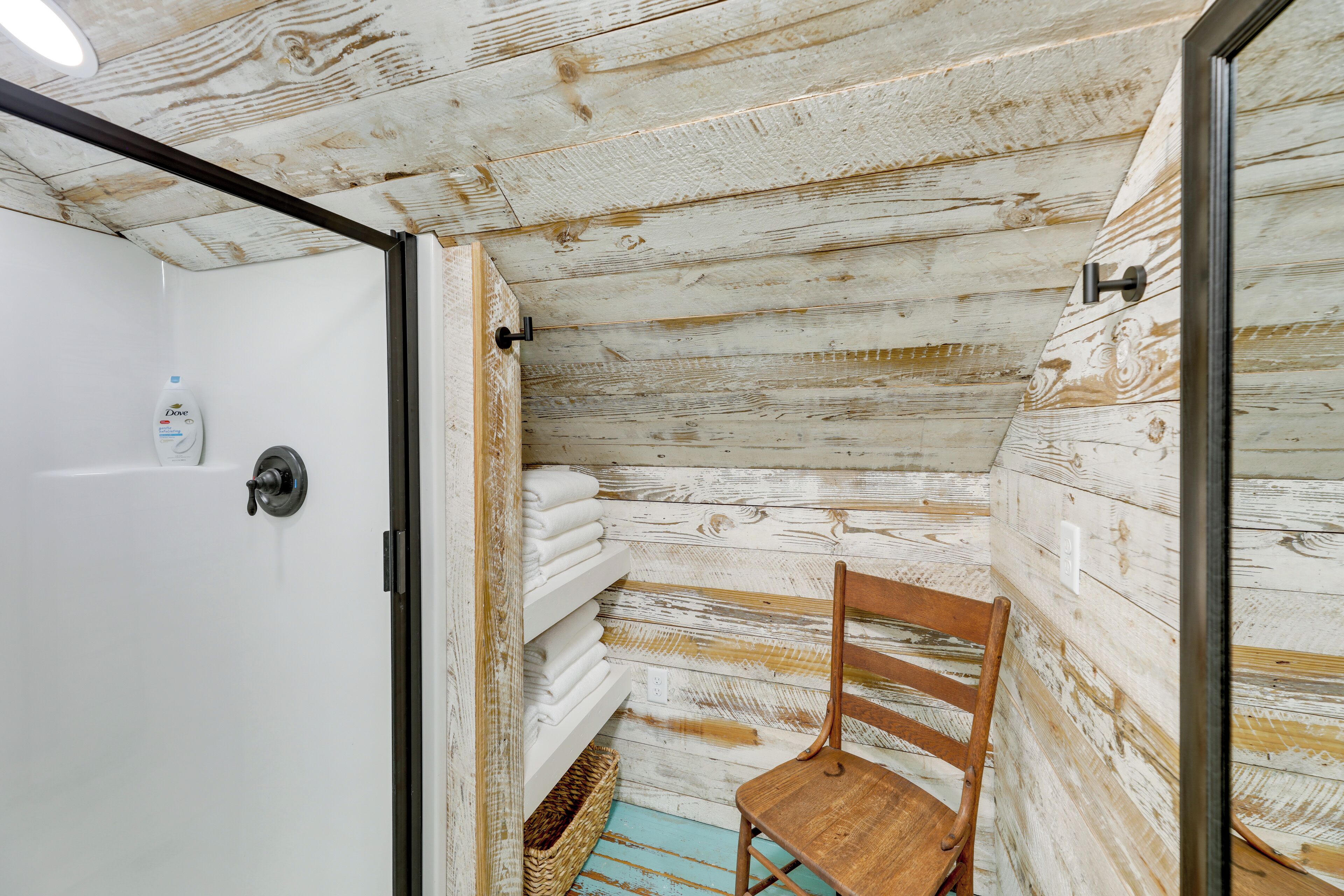 Une salle de bain rustique avec des murs en bois, une porte blanche, une chaise en bois et des serviettes soigneusement pliées sur une étagère.