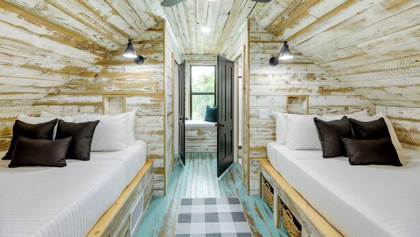 A rustic wooden room with two beds, a checkered rug, and a ceiling fan. - Sip, Fish & Relax Fireside: Serene Schulenburg Gem (Schulenburg)