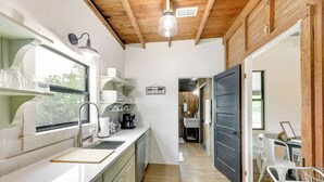 A modern kitchen with white cabinets, a wooden ceiling, and a view through an open door to a dining area. - Sip, Fish & Relax Fireside: Serene Schulenburg Gem (Schulenburg)