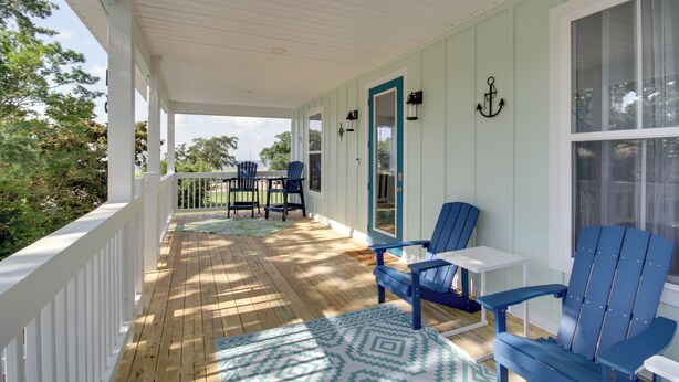 Une véranda couverte avec un plancher en bois, des fauteuils Adirondack bleus, une petite table et une vue sur la verdure environnante.