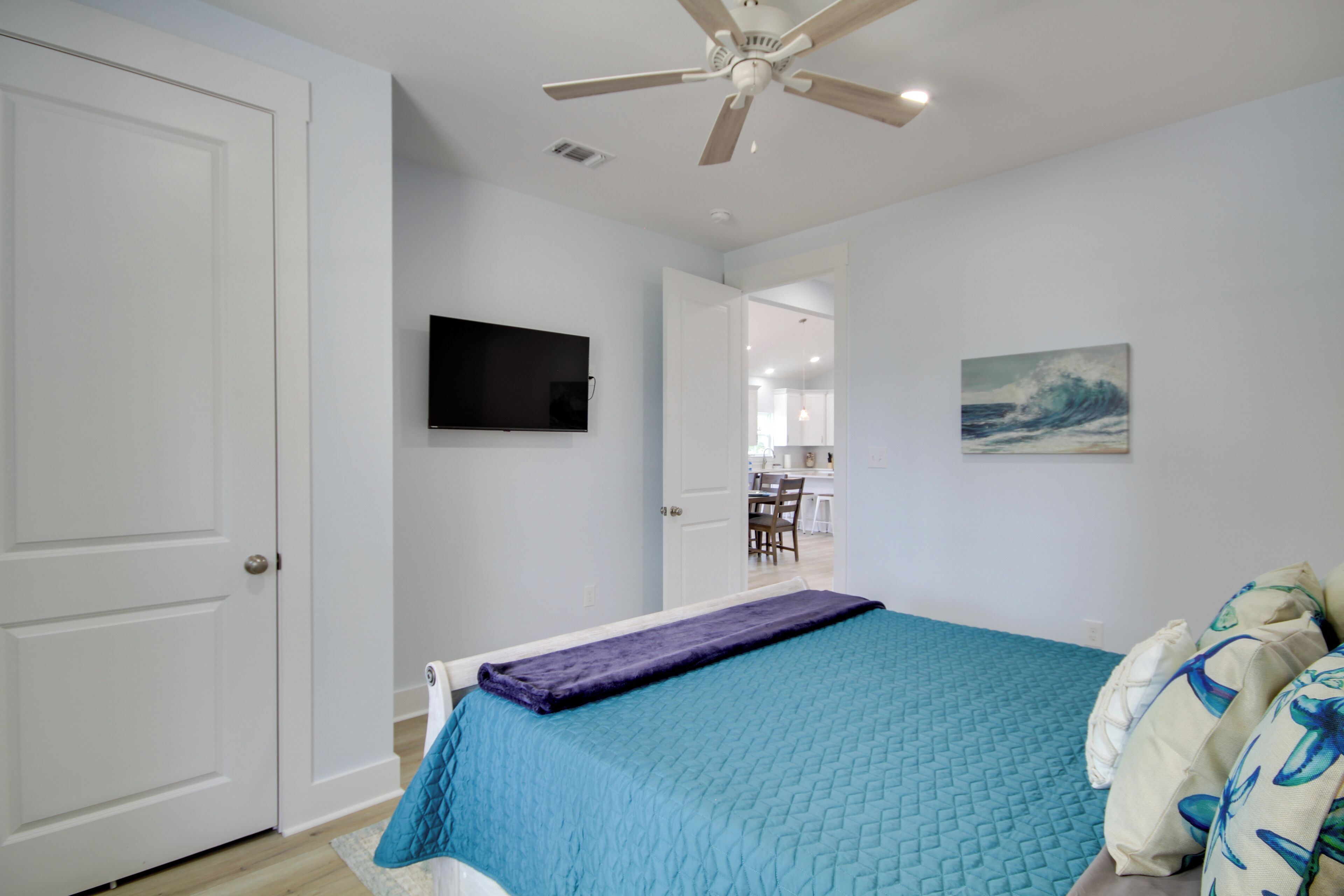 A bedroom with a bed, a ceiling fan, a TV, and a painting on the wall.