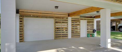 Un garaje techado con puerta blanca, listones de madera y suelo de concreto.