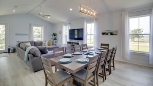 Un salon spacieux comprenant un coin repas, de grandes fenêtres et un ventilateur de plafond.