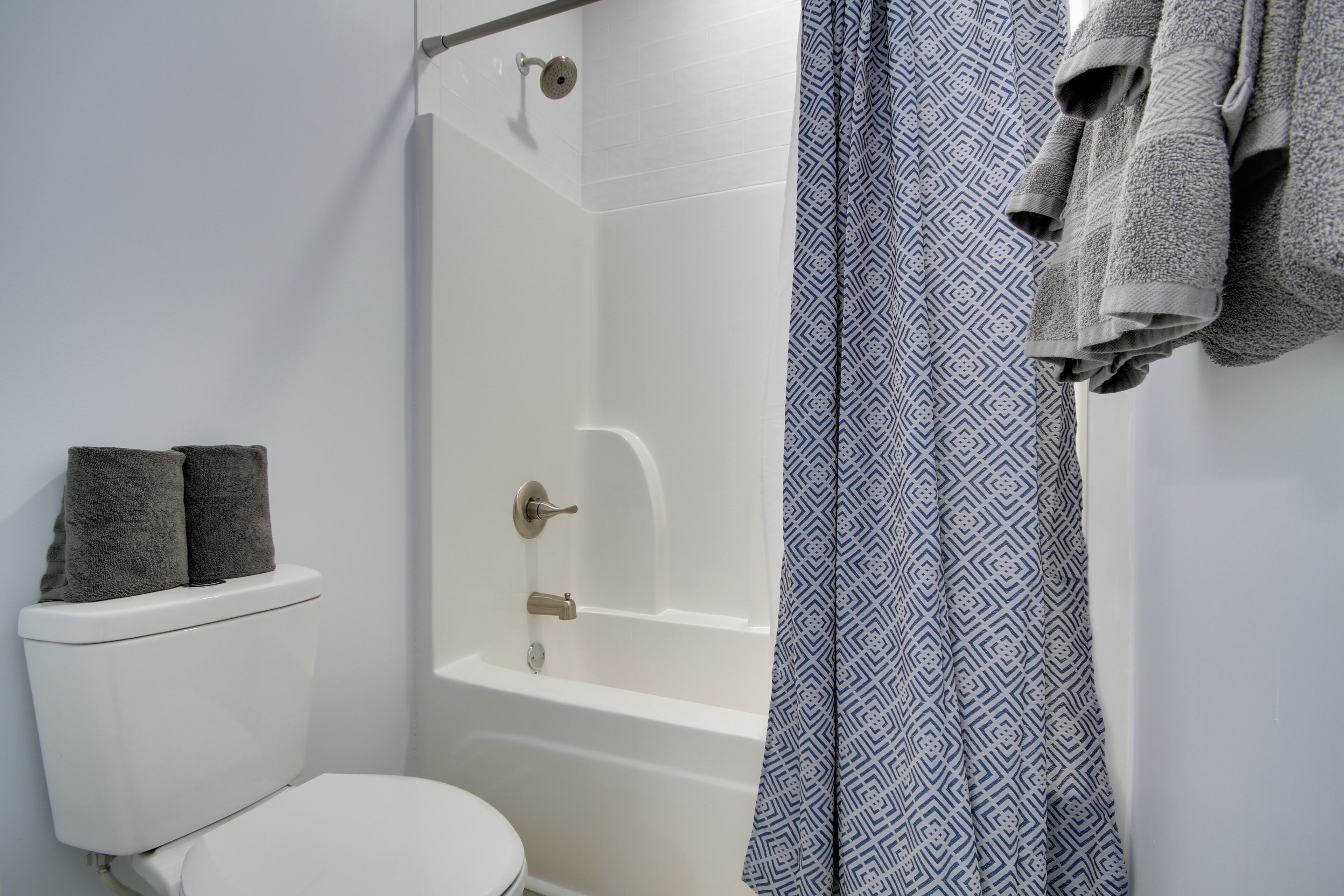 Un baño con inodoro blanco, ducha y cortina de ducha estampada.