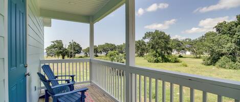 A covered porch with two Adirondack chairs and a view of a grassy yard with trees.