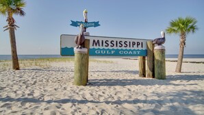 Un panneau sur une plage de sable, avec deux pélicans perchés au sommet, portant l’inscription « Côte du golfe du Mississippi ».