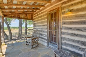 Une cabane en rondins avec une véranda dallée de pierres, une chaise berçante et une grande fenêtre.