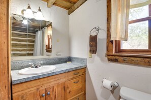 Un baño con tocador de madera, lavamanos e inodoro.