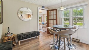 Ein Essbereich mit einem runden Tisch, Barhocker, einer Holzbank, einem schwarzen Koffer und einem Spiegel an der Wand.