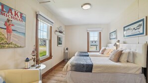 Ein Schlafzimmer mit einem großen Bett, einem kleinen Tisch, einem Stuhl und einem Gemälde vom Michigansee.