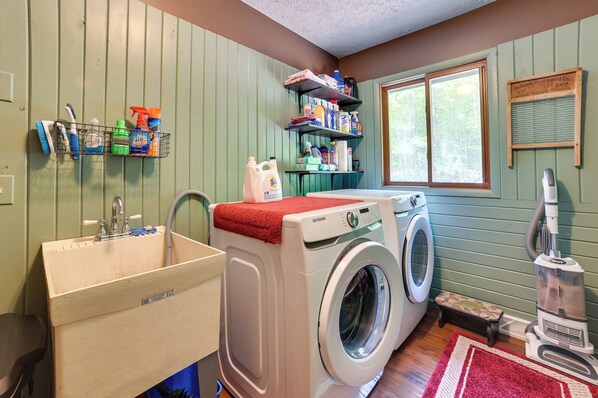 A laundry room with a washing machine, a sink, shelves with cleaning supplies, and a vacuum cleaner.