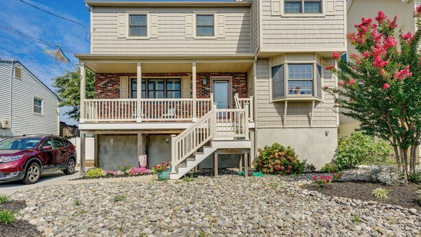 A two-story house with a front porch, a garage, and a small front yard with rocks and plants. - Brigantine Vacation Rental w/ Private Pool! (Brigantine)
