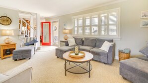 A living room with a grey sofa, ottoman, and coffee table, a red door, and a staircase leading to another room. - Brigantine Vacation Rental w/ Private Pool! (Brigantine)