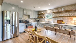 Une cuisine moderne dotée d’appareils électroménagers en acier inoxydable, de meubles de rangement en bois clair et d’un mur d’accent en pierre.