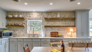 Une cuisine avec des murs en pierre, des étagères en bois, une table à manger avec des chaises et un four à micro-ondes.