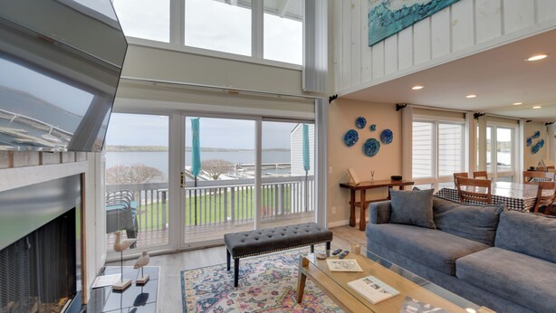 A spacious living room with a large glass door leading to a balcony, a fireplace, a sofa, and a coffee table. - Luxury Lakefront Boyne City Townhome w/ Views! (Boyne City)
