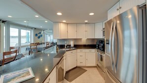 A modern kitchen with white cabinets, stainless steel appliances, and a large island with a welcome mat. - Luxury Lakefront Boyne City Townhome w/ Views! (Boyne City)
