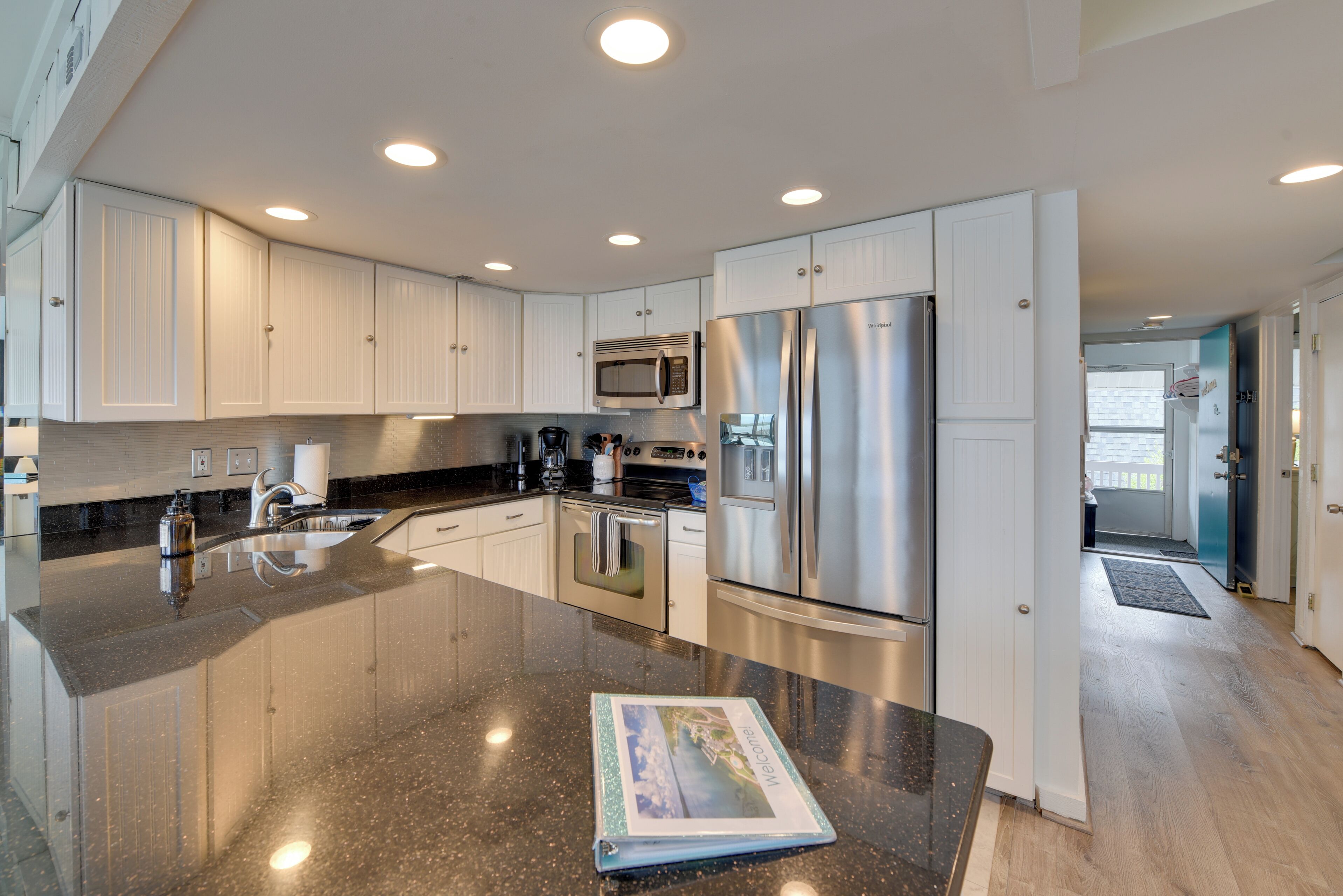 A modern kitchen with stainless steel appliances, white cabinetry, and a granite countertop.
