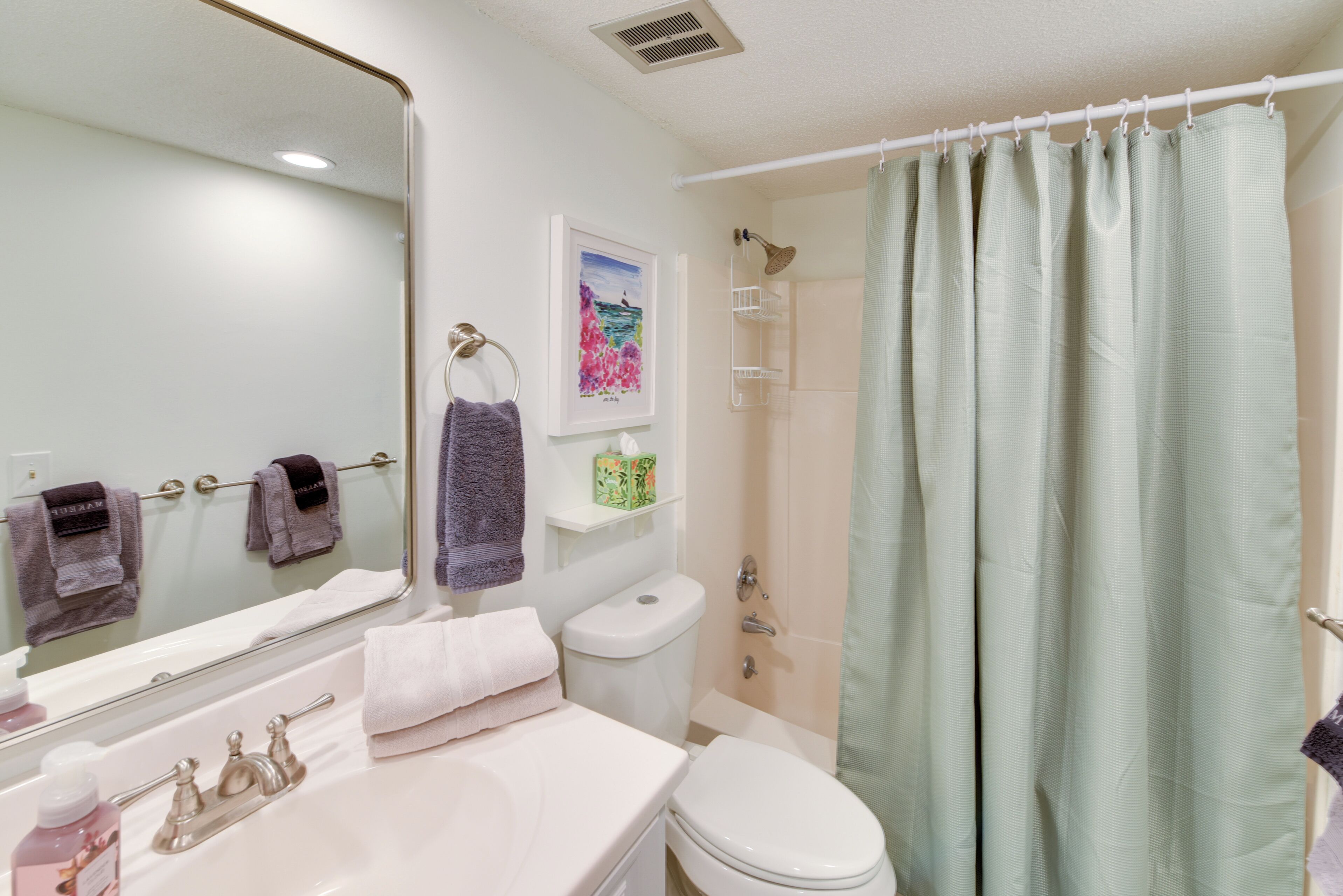 A bathroom with a sink, mirror, toilet, and shower curtain.