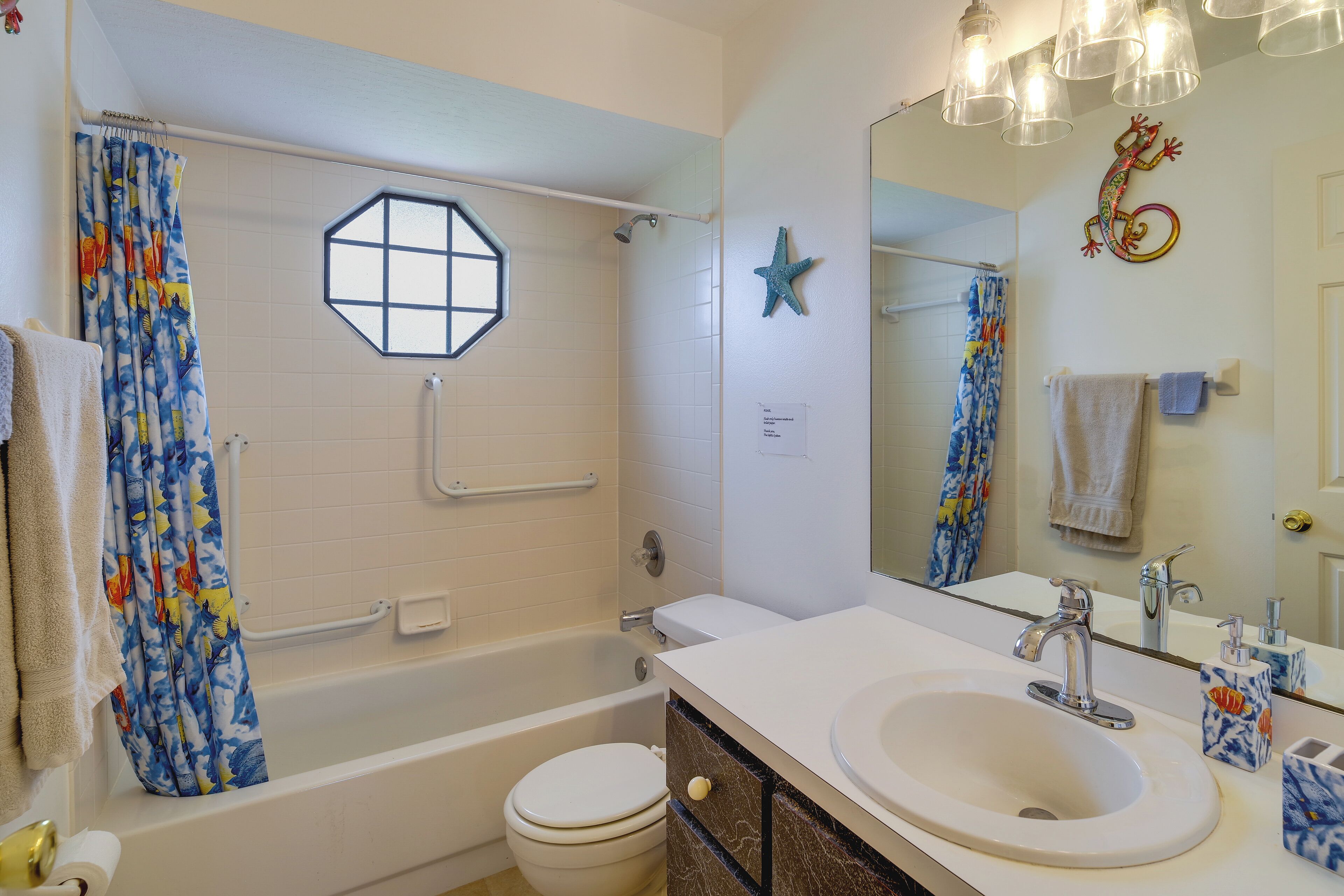 A bathroom with a bathtub, toilet, and sink. There is a shower curtain, a starfish decoration, and a mirror with lights above the sink.