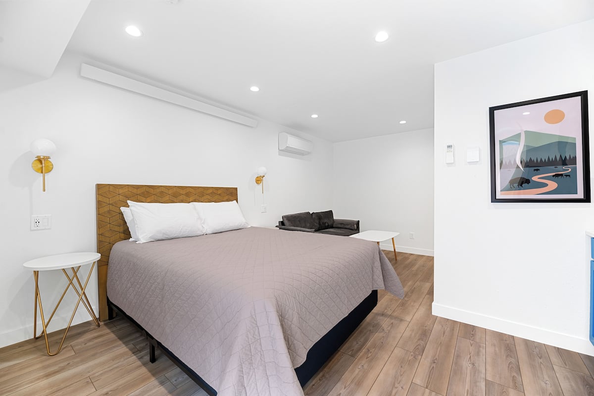 A modern bedroom with a large bed, a headboard, a bedside table, a wall-mounted air conditioner, and a framed picture on the wall.