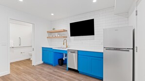 A modern kitchen with white and blue cabinetry, a built-in dishwasher, and a large refrigerator. - Queen City Inn (Spearfish)