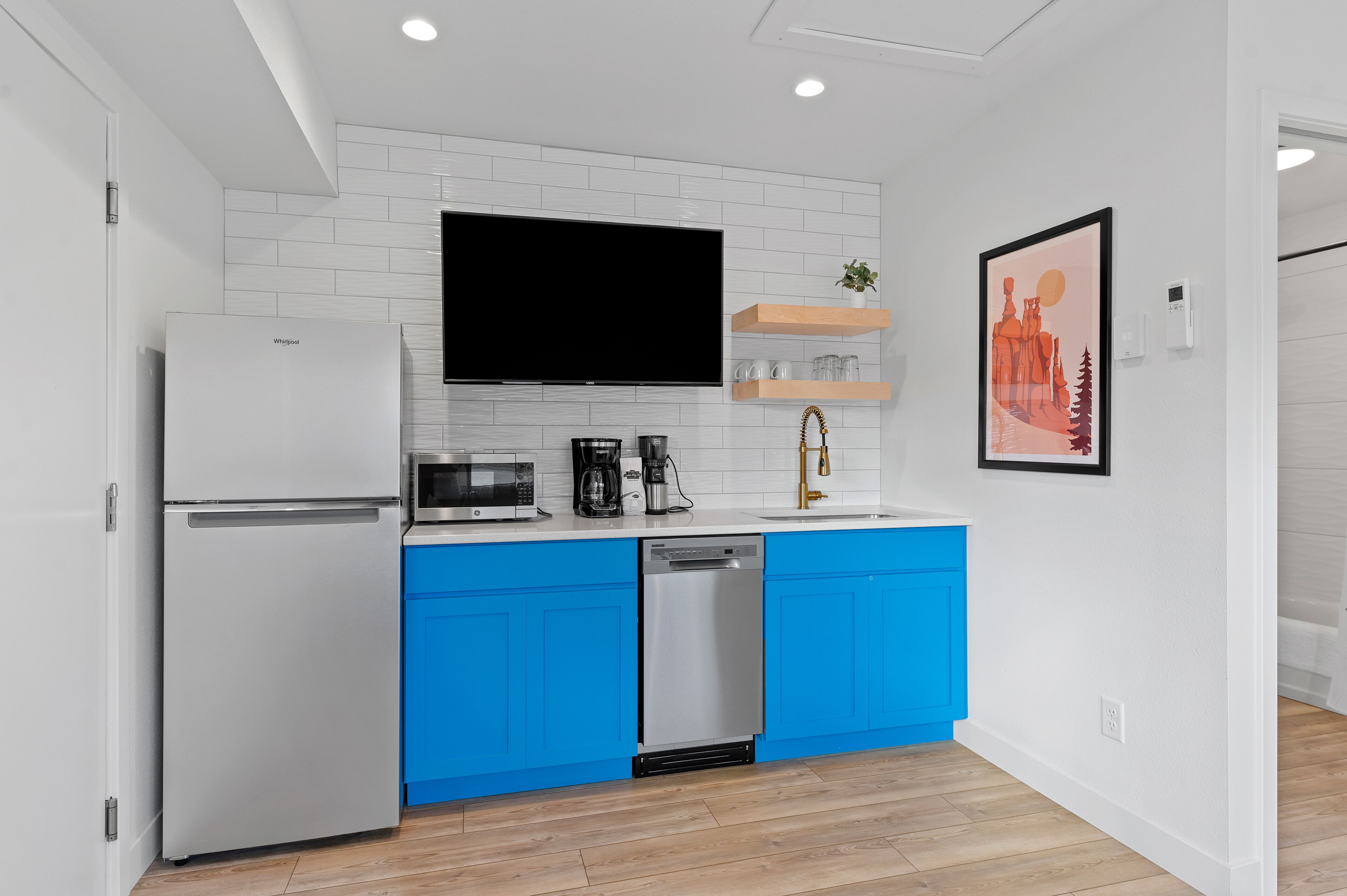Una cocina moderna con armarios blancos y azules, un microondas integrado, una cafetera y un lavavajillas.
