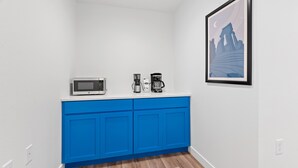 A kitchen with white walls, blue cabinets, and a framed picture on the wall. - Queen City Inn (Spearfish)