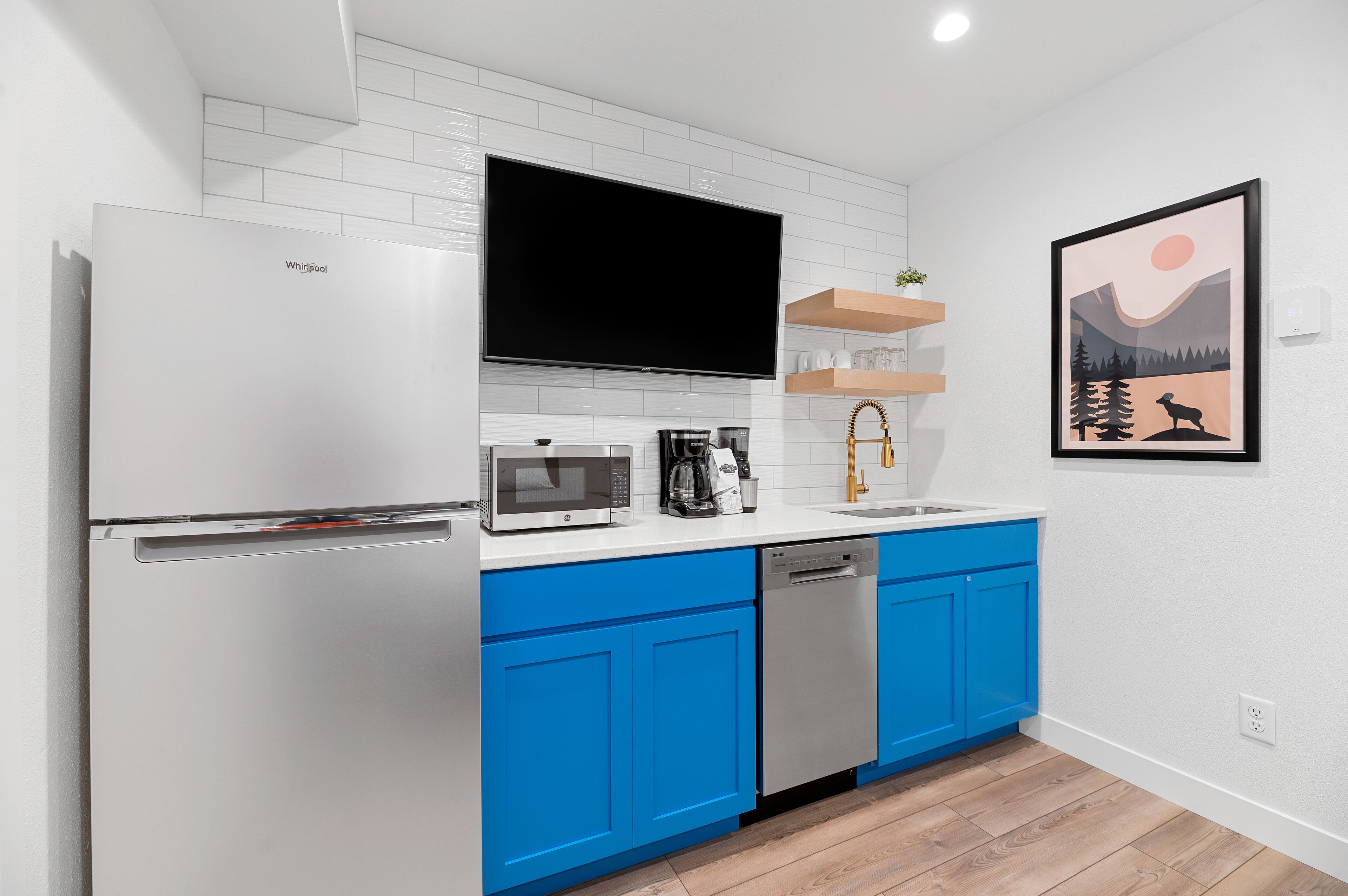 A modern kitchen with a white refrigerator, blue cabinets, a microwave, a coffee maker, and a dishwasher.