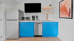 A modern kitchen with a white refrigerator, a microwave, a coffee maker, and a dishwasher. There is a TV mounted above the counter and a framed picture on the wall. - Queen City Inn (Spearfish)