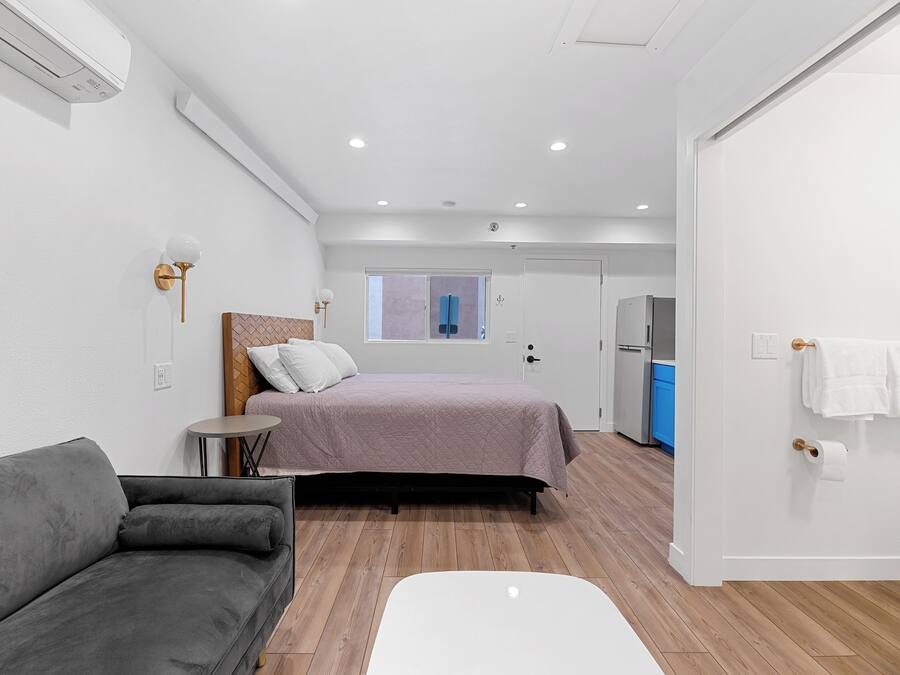 Un dormitorio moderno con una cama, un sofá gris, una mesita pequeña y una silla blanca.