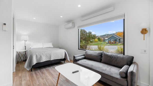 A modern bedroom with a bed, a gray sofa, and a white coffee table. - Queen City Inn (Spearfish)