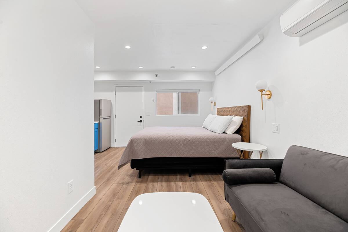 A modern bedroom with a bed, a gray sofa, a small round table, and a white wall.