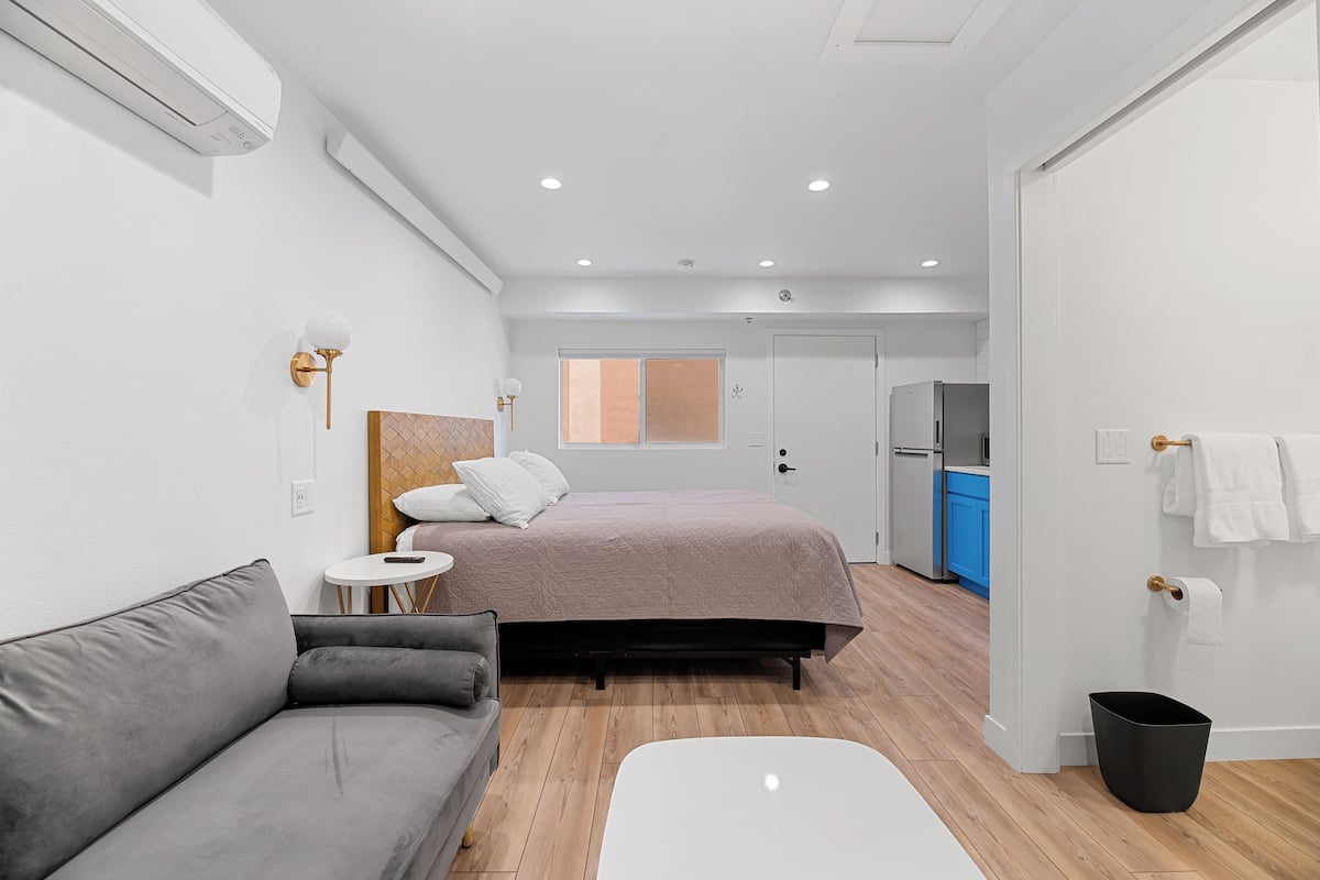 A modern bedroom with a bed, a grey sofa, a small round table, and a white bedside table.