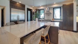 Een moderne keuken met een groot kookeiland, donkere kastjes en hangende lampen.