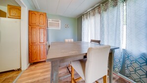 A dining area with a wooden table and chairs, a white refrigerator, wooden cabinets, and a patterned curtain. - Cozy Geneva Home: Walk to Lake Erie & Main Strip! (Geneva)