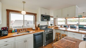 A modern kitchen with white cabinets, a stainless steel stove, and a large window providing a view of the outside. - Ocean-view Apt in the Heart of Southwest Harbor! (Southwest Harbor)