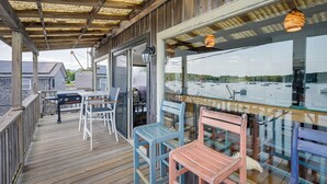 A wooden deck with a glass railing overlooking a body of water, featuring outdoor seating and a grill. - Ocean-view Apt in the Heart of Southwest Harbor! (Southwest Harbor)