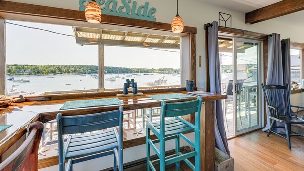 A dining area with a view of the water, wooden furniture, and a sign reading "SeaSide". - Ocean-view Apt in the Heart of Southwest Harbor! (Southwest Harbor)