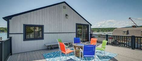 A deck with a wooden floor, a small building with a window, and colorful chairs.