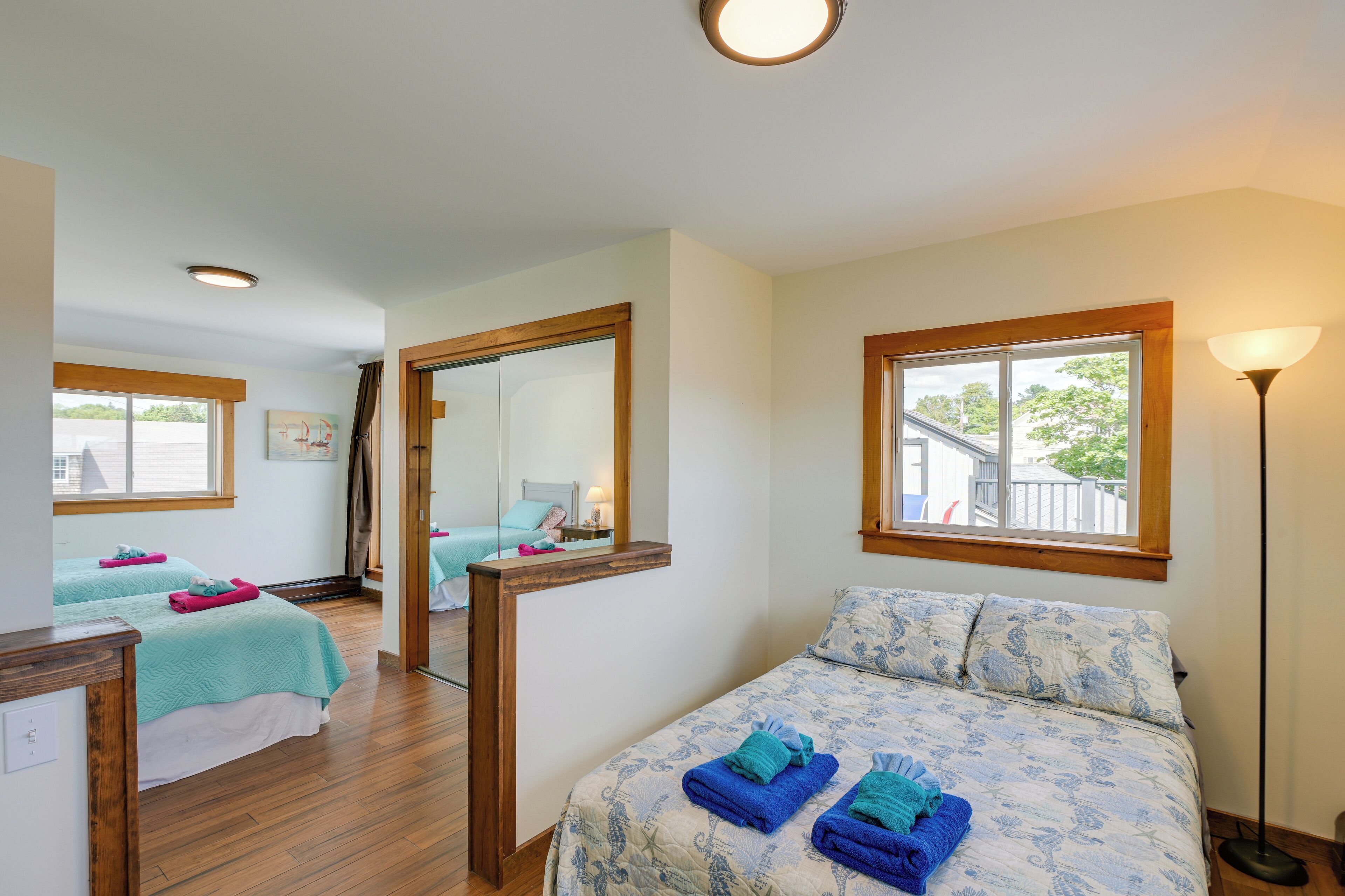 A hotel room with two beds, a large mirror, a window with a view, and a floor lamp.