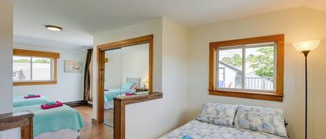 A hotel room with two beds, a large mirror, a window with a view, and a floor lamp.