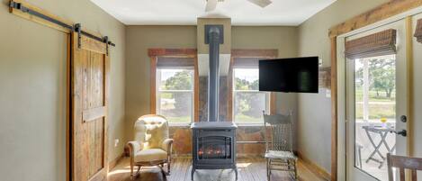A cozy room with a wood-burning stove, a ceiling fan, and a TV mounted on the wall.