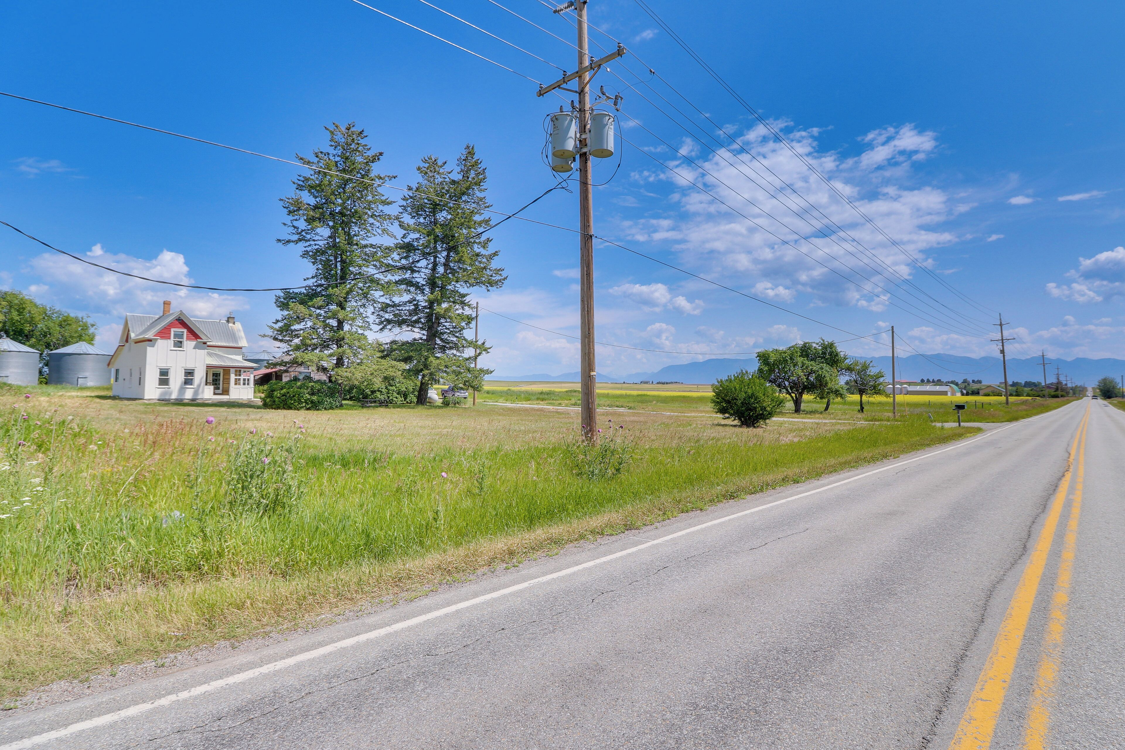 Une route de campagne avec une maison sur le côté gauche, entourée de verdure et sous un ciel dégagé.