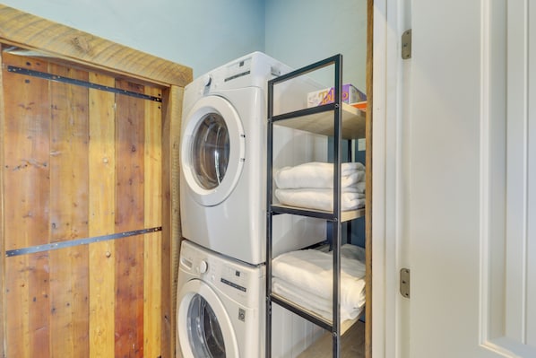 A laundry room with stacked washers and dryers, a wooden door, and a shelf with folded towels.