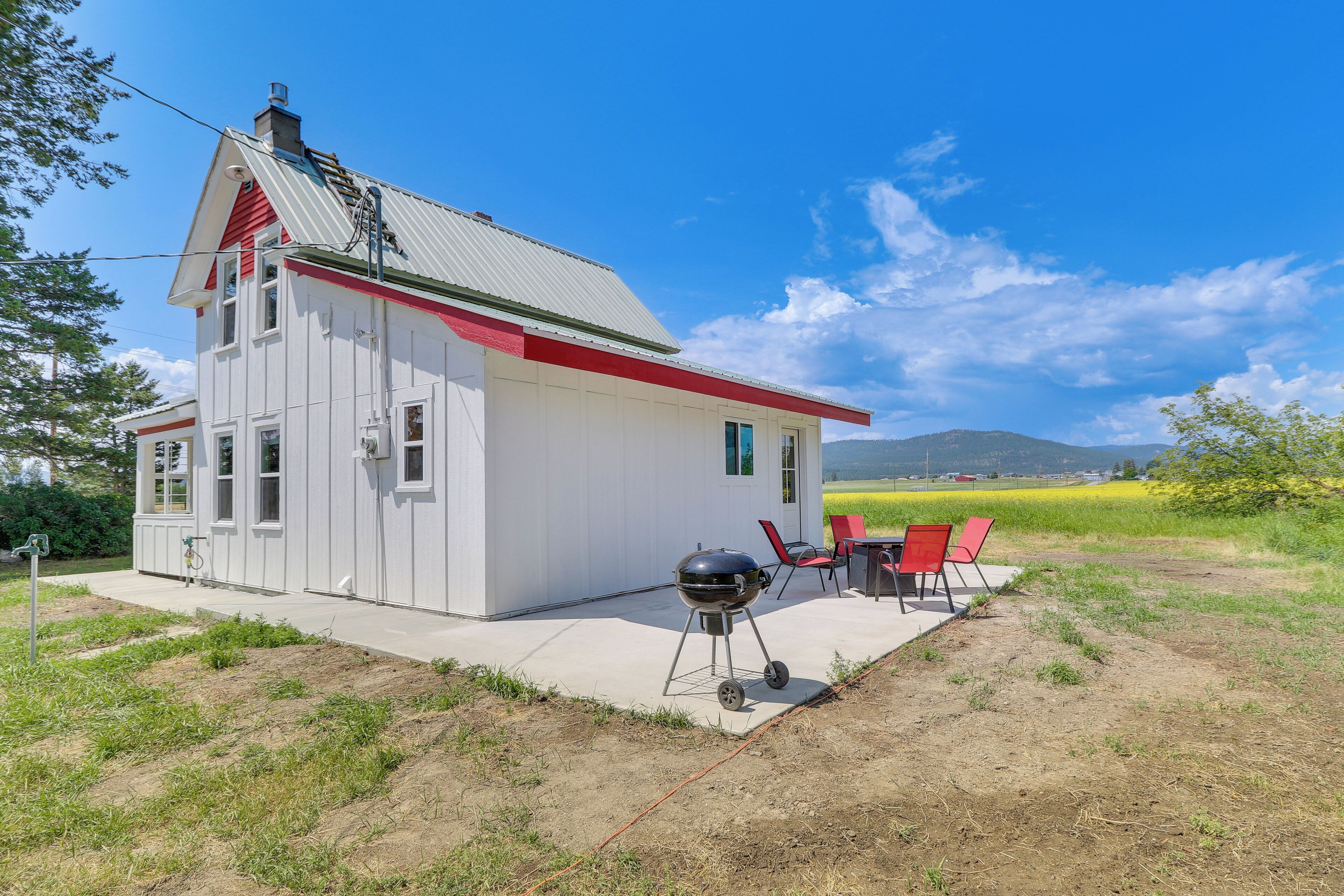 A white house with a red roof and chimney, a barbecue grill, and red chairs outside.